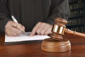 A gavel and block rests on a judge's desk while the magistrate takes notes in his law library preparing to oversee a case.