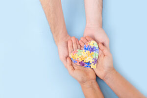two hands holding a rainbow heart signifying autism