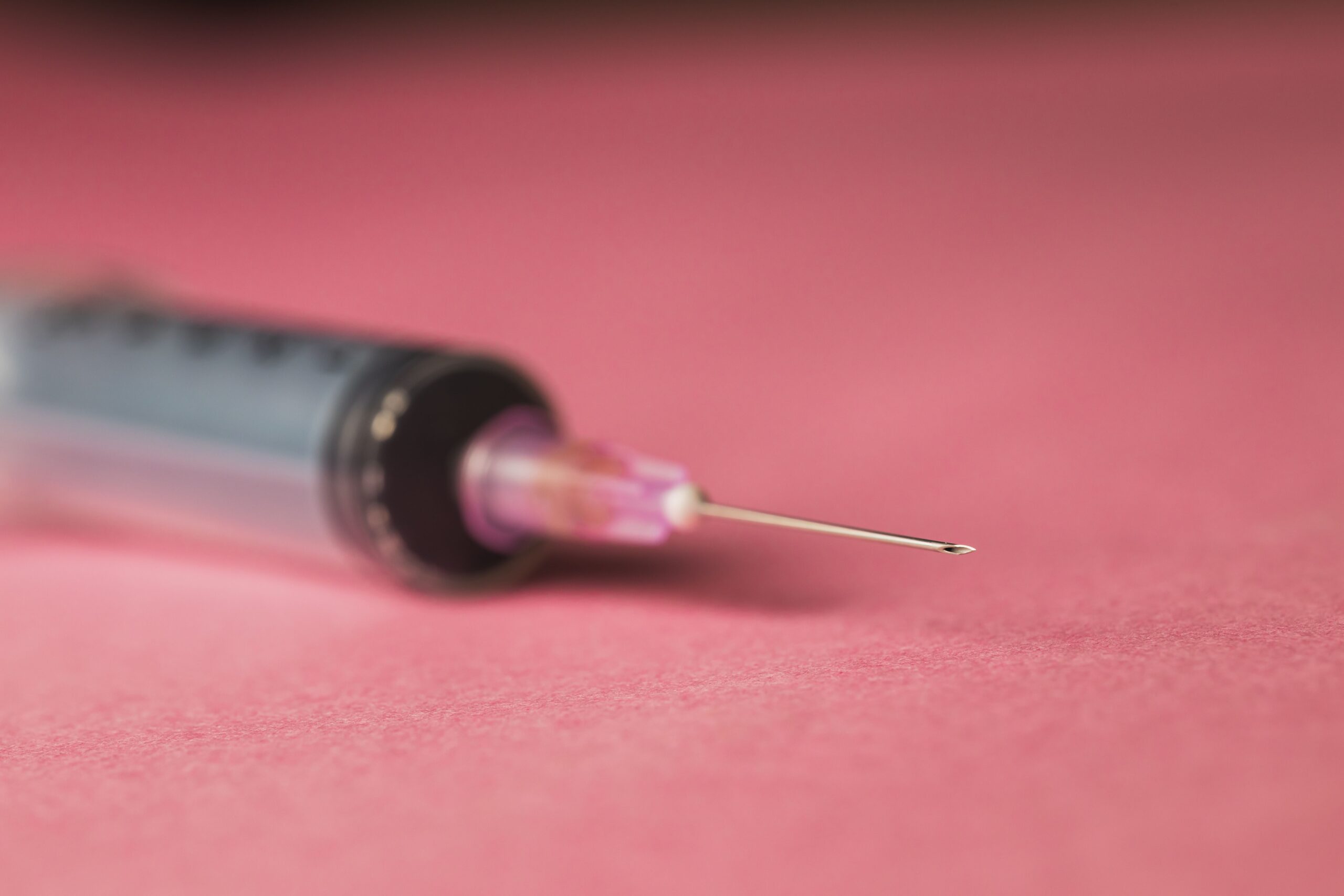 A closeup of a syringe with a needle on a pink background