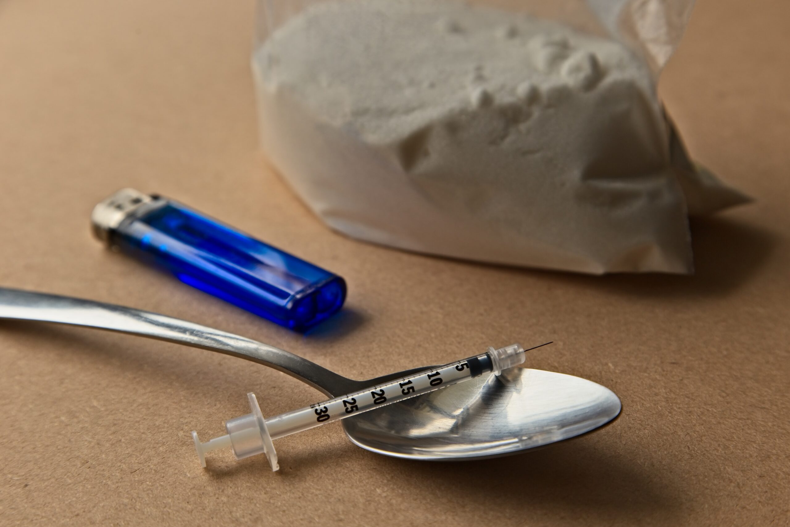 Drug abuse concept image consisting of a spoon, syringe, lighter and a bag of heroin.