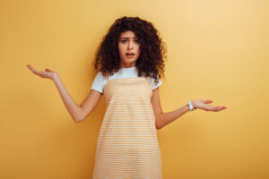 shocked, offended mixed race girl looking at camera while standing with open arms on yellow