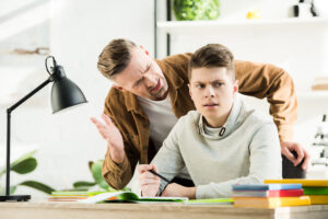 angry father gesturing and screaming at teen son, boy covering ears