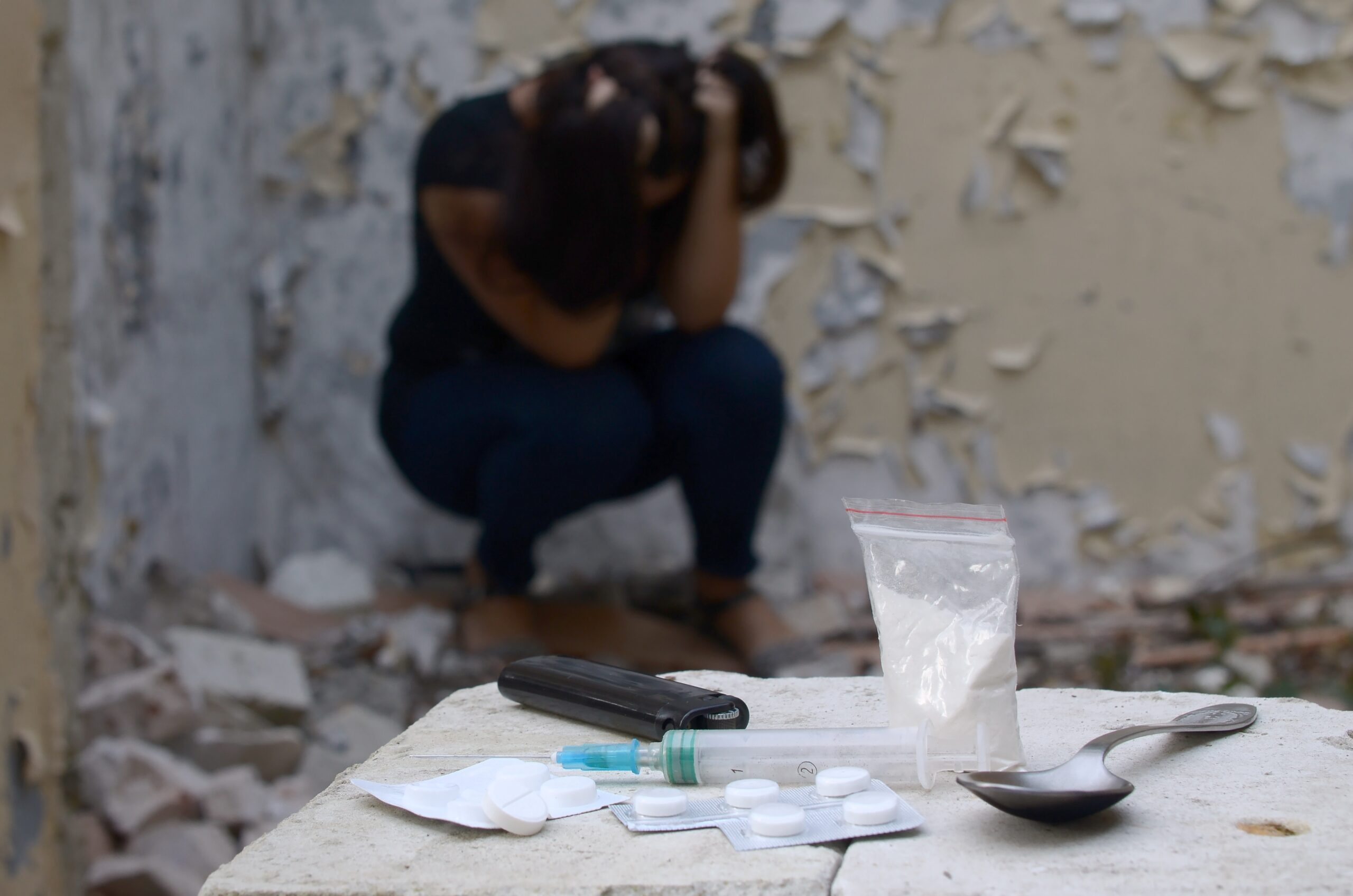 Young woman in despair suffers from narcotic effects next to packs of heroin and many drug tablets. Problems of drug addiction and illegal narcotic trafficking