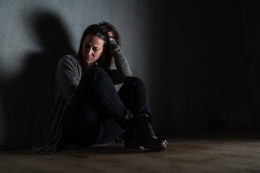 A sad mid-adult woman, alone in darkness, sitting and thinking.