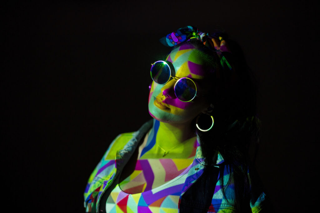 Pretty woman in sunglasses with geometric colored face and body with light.
