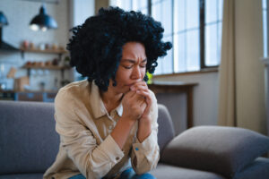 Depressed oppressed African American woman sits on couch in room waiting for psychologist flying psychological problems. Sad offended girl crying suffering from depression and stress