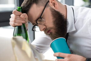 drunk businessman with bottle of champagne sleeping at workplace