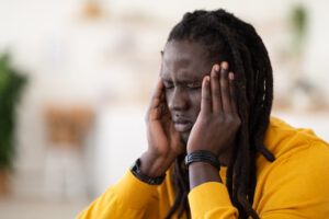 Closeup Shot Of Stressed Black Young Man Suffering From Headache At Home, Millennial African American Guy Frowning And Touching Temples, Having Acute Migraine, Selective Focus With Free Space