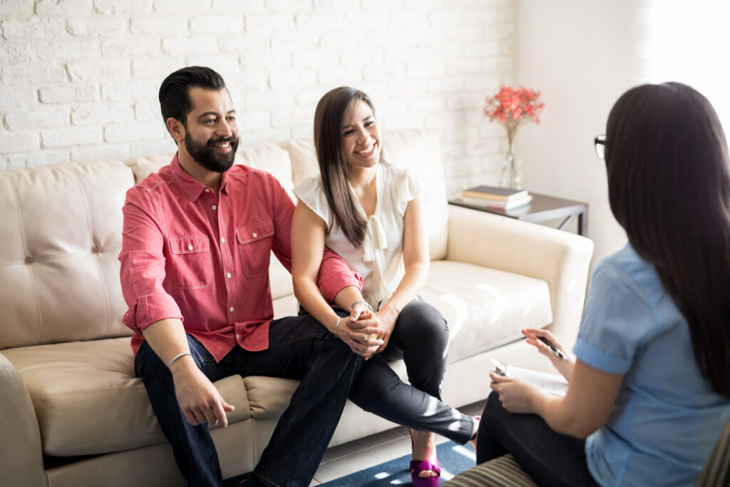 Hispanic couple sitting close to each other and holding hands while looking at their therapist