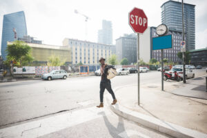 Young handsome afro man walking outdoor in the city holding a bag crossing street - traveler, strolling concept