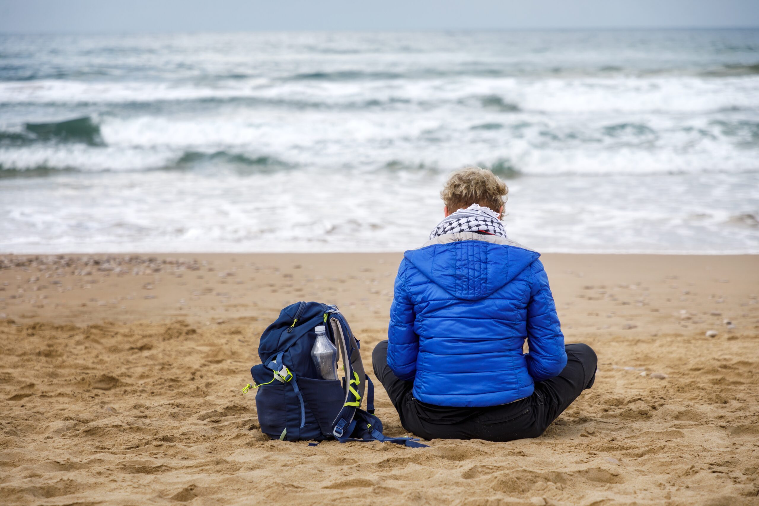 woman sitting alone on the beach in a blue jacket