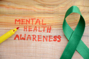 Red lettering "MENTAL HEALTH AWARENESS" and green ribbon on the wooden surface