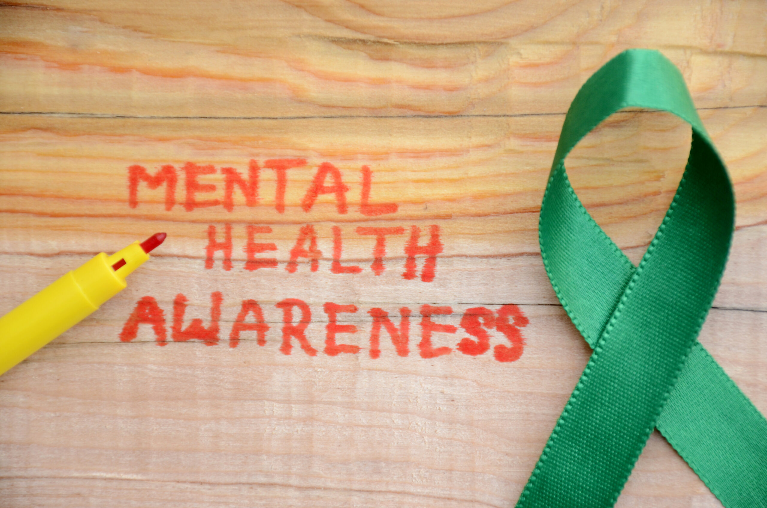Red lettering "MENTAL HEALTH AWARENESS" and green ribbon on the wooden surface