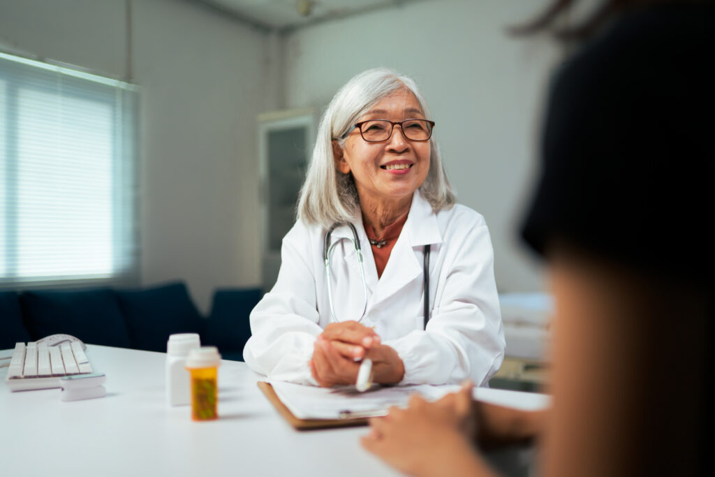 Senior Asian doctor smiling, listening to a patient in a medical clinic