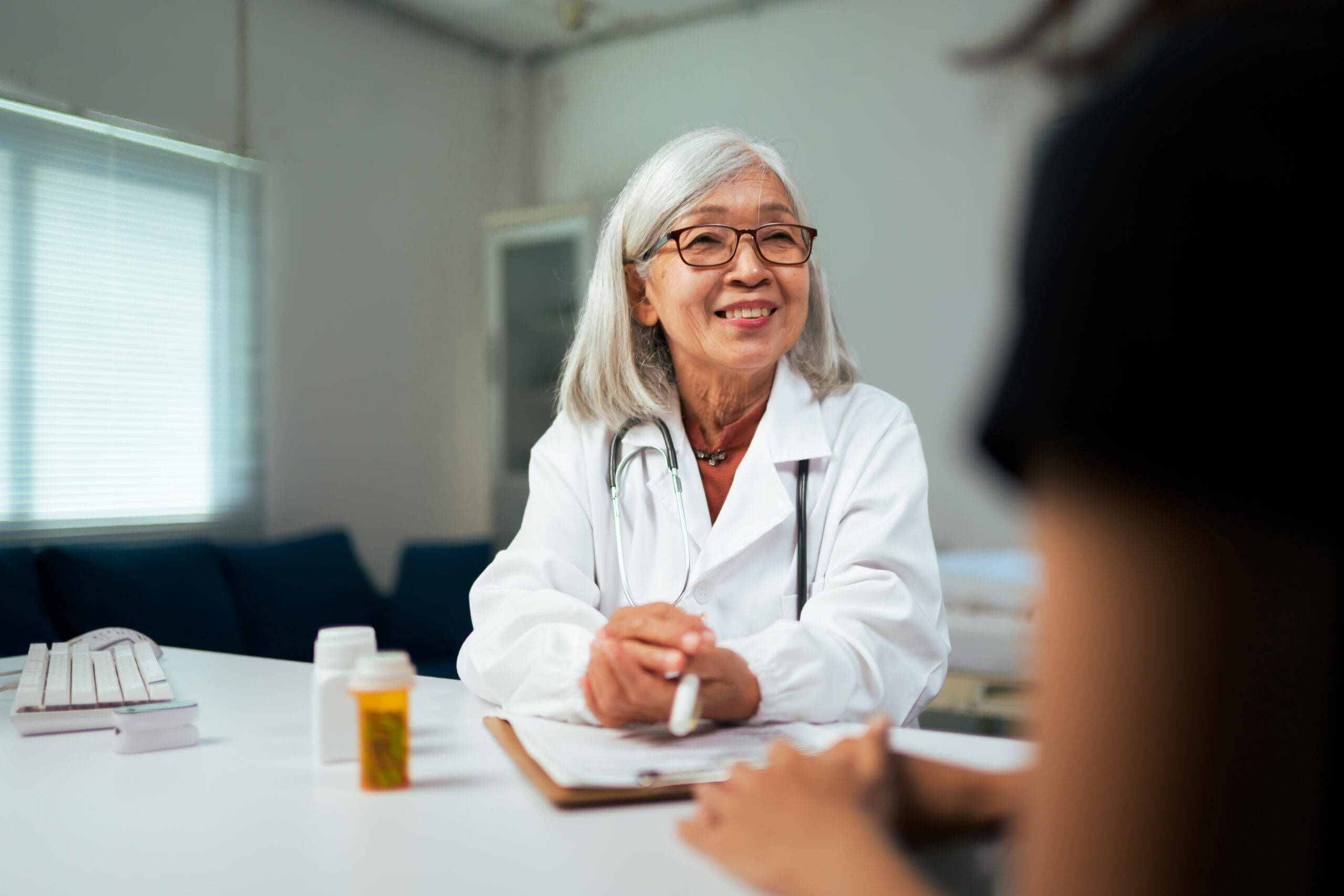 Senior Asian doctor smiling, listening to a patient in a medical clinic
