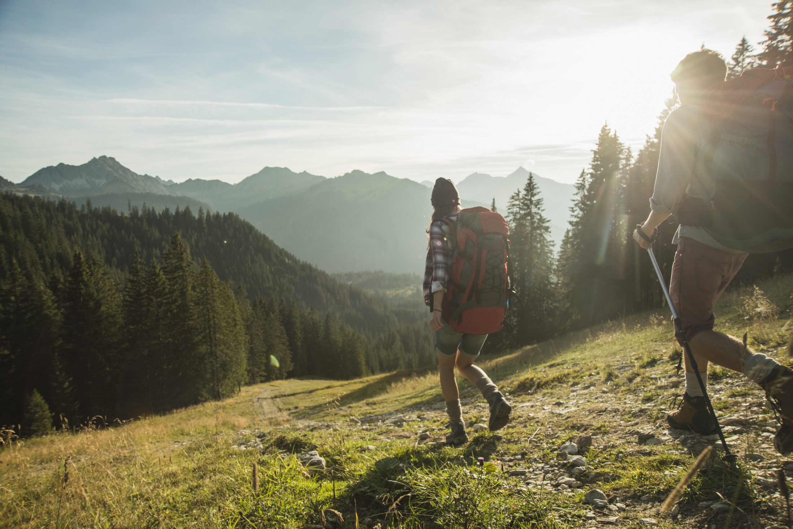 Austria, Tyrol, Tannheimer Tal, young couple hiking in sunlight on alpine meadow